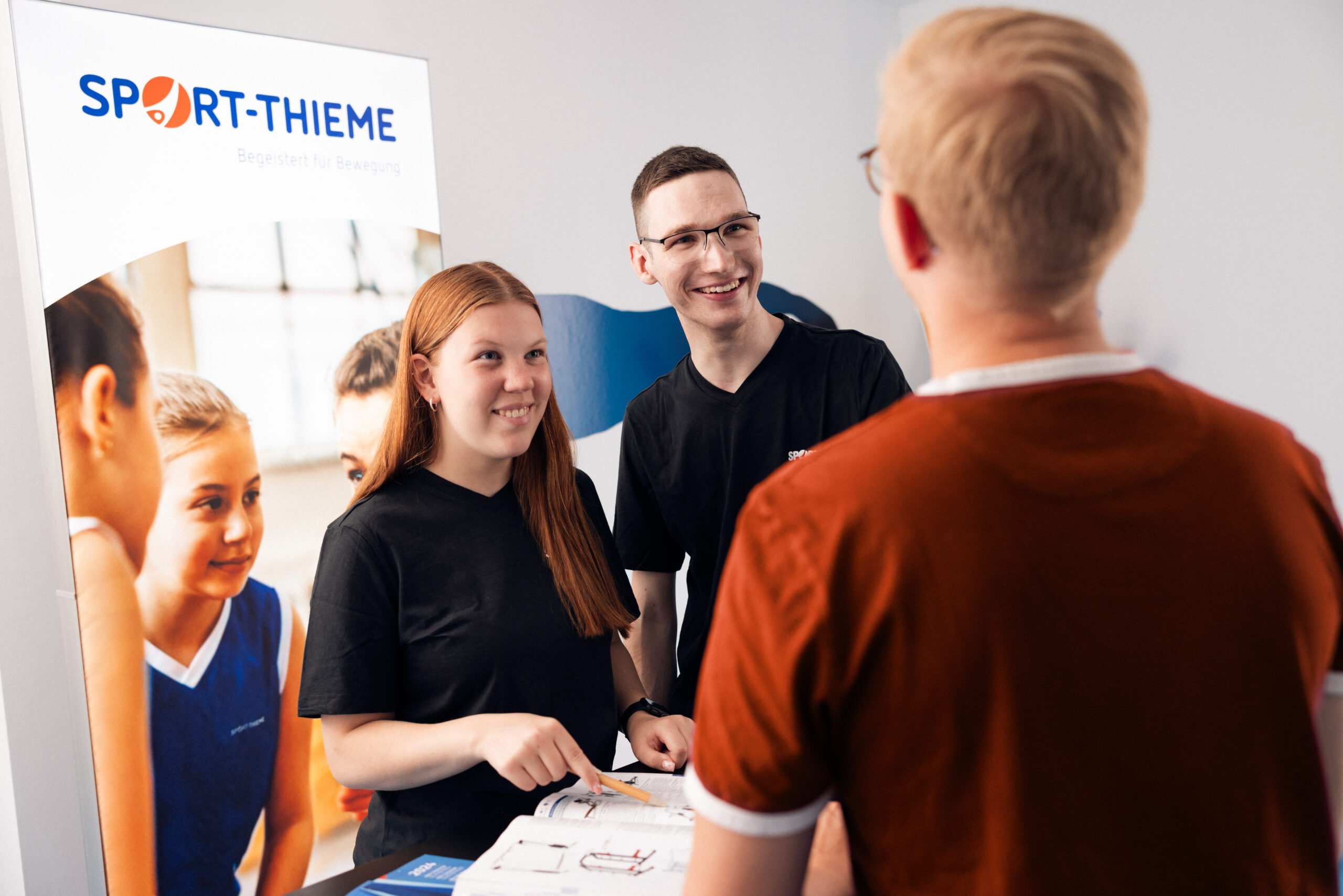 Mitarbeitende von Sport-Thieme im Gespräch mit Besuchenden an einem Messestand in moderner, einladender Umgebung