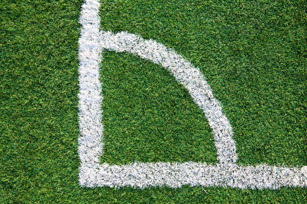 Nahaufnahme einer weißen Eckmarkierung auf einem Fußballfeld aus Kunstrasen.