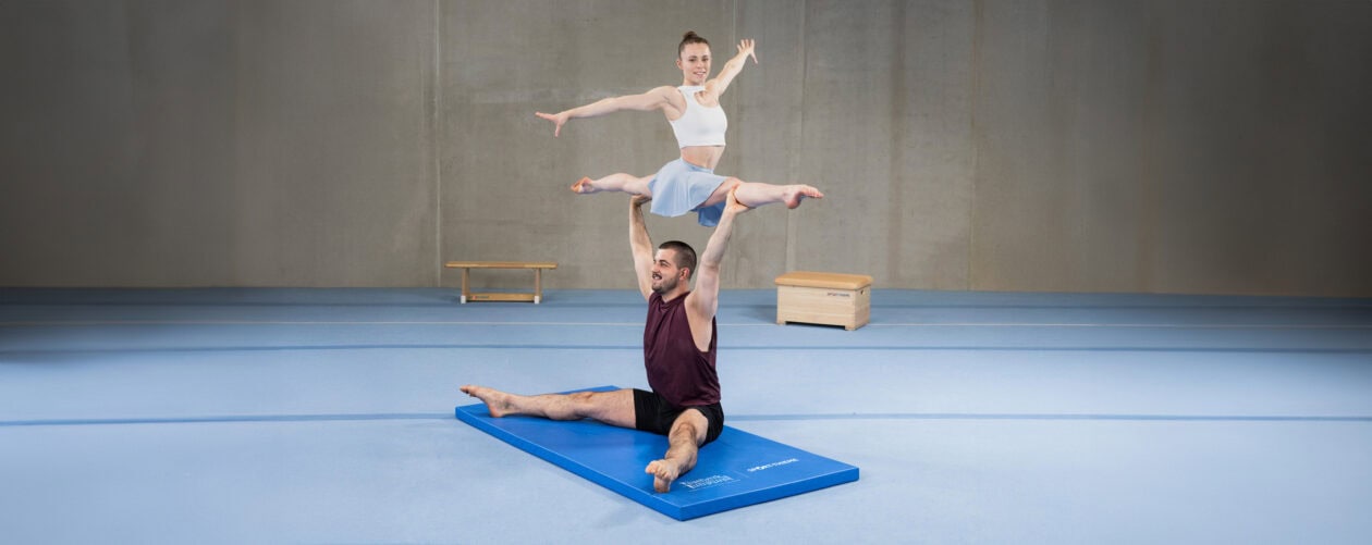 Two athletes performing gymnastics exercises on a mat