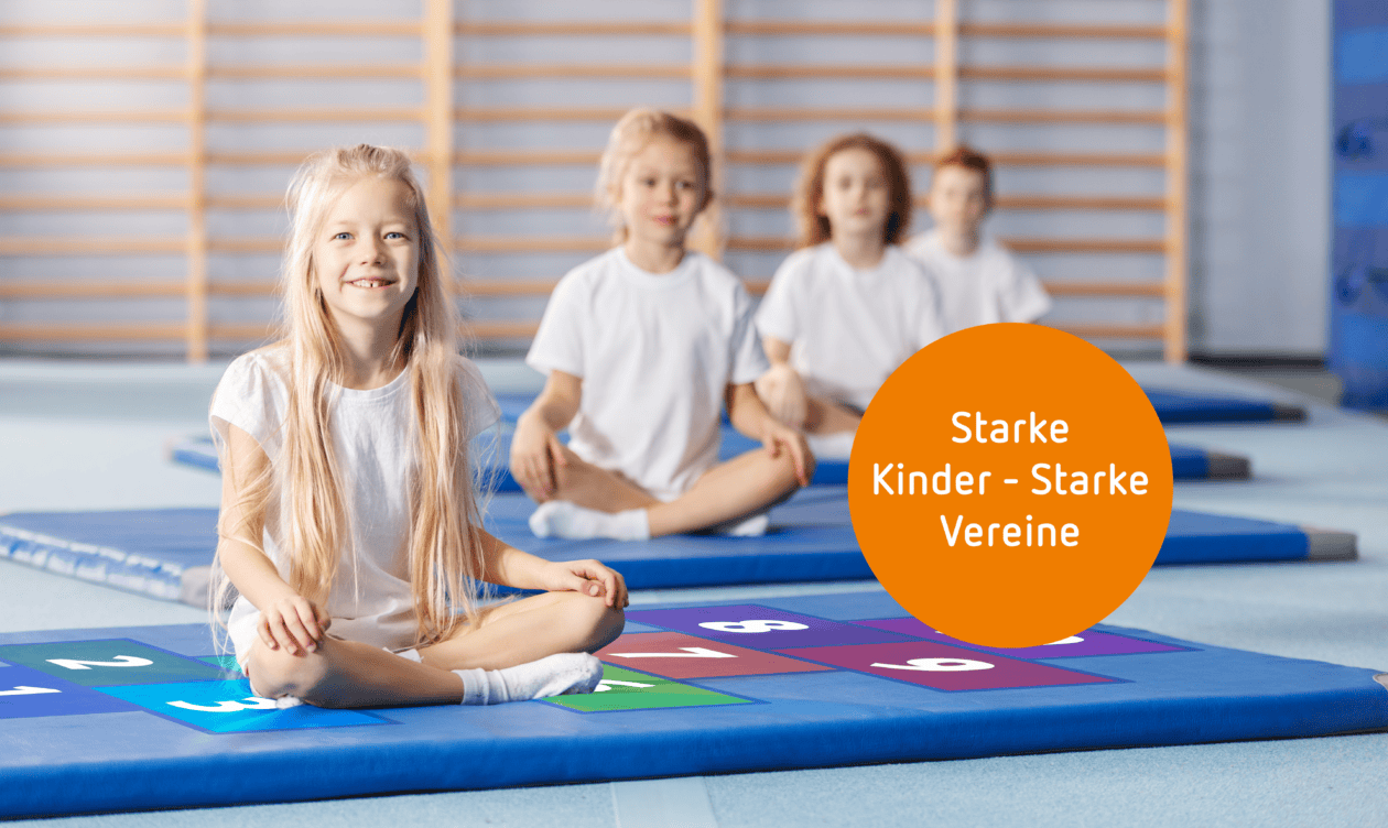 Kinder sitzen auf blauen Turnmatten in einer Sporthalle. Im Bild steht „Starke Kinder – Starke Vereine“.